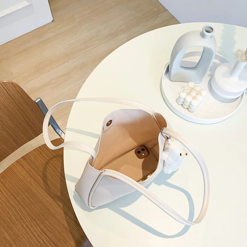 حقيبة كتف أو حقيبة يد صغيرة أنيقة وعملية من الجلد الصناعي، بتصميم عصري وجذاب، مزينة بقلادة على شكل دب.